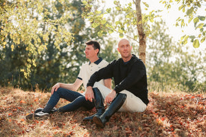 Two men sitting on a grassy hill with trees in the background