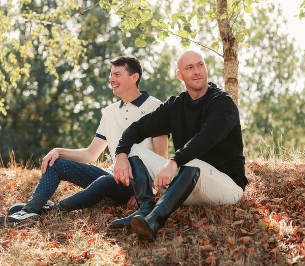 Two men sitting on a grassy hill with trees in the background