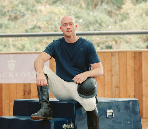 Man sitting on equestrian training blocks with a helmet and boots, outdoors.