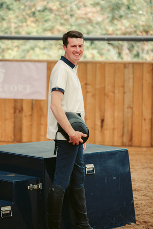 Man holding a helmet in an equestrian setting with a wooden fence and grass in the background.