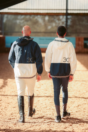 Two people wearing equestrian jackets and riding boots walking on a dirt path.