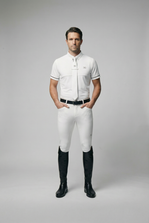 Male model wearing white mens show shirt with black breeches and riding boots standing against grey background