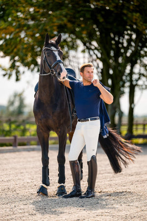 Man in equestrian attire standing next to a horse in an outdoor setting