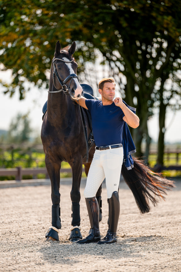 Man in equestrian attire standing next to a horse in an outdoor setting