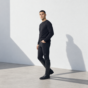 Mens Breeches in black stretch fabric, close-fitting with a subtle logo and full-length legs tucked into riding boots.