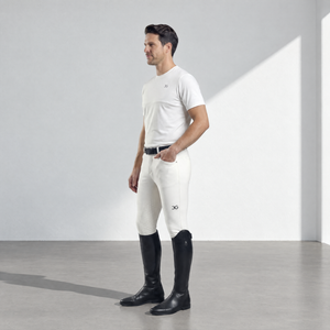 Mens Breeches in bone-colored stretch fabric, with a close fit, subtle thigh logo, and black knee-high riding boots.